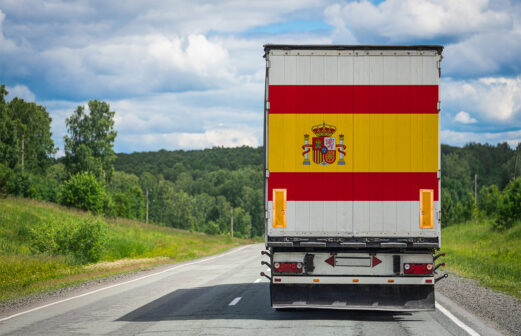 A  truck with the national flag of Spain depicted on the back door carries goods to another country along the highway. Concept of export-import,transportation, national delivery of goods